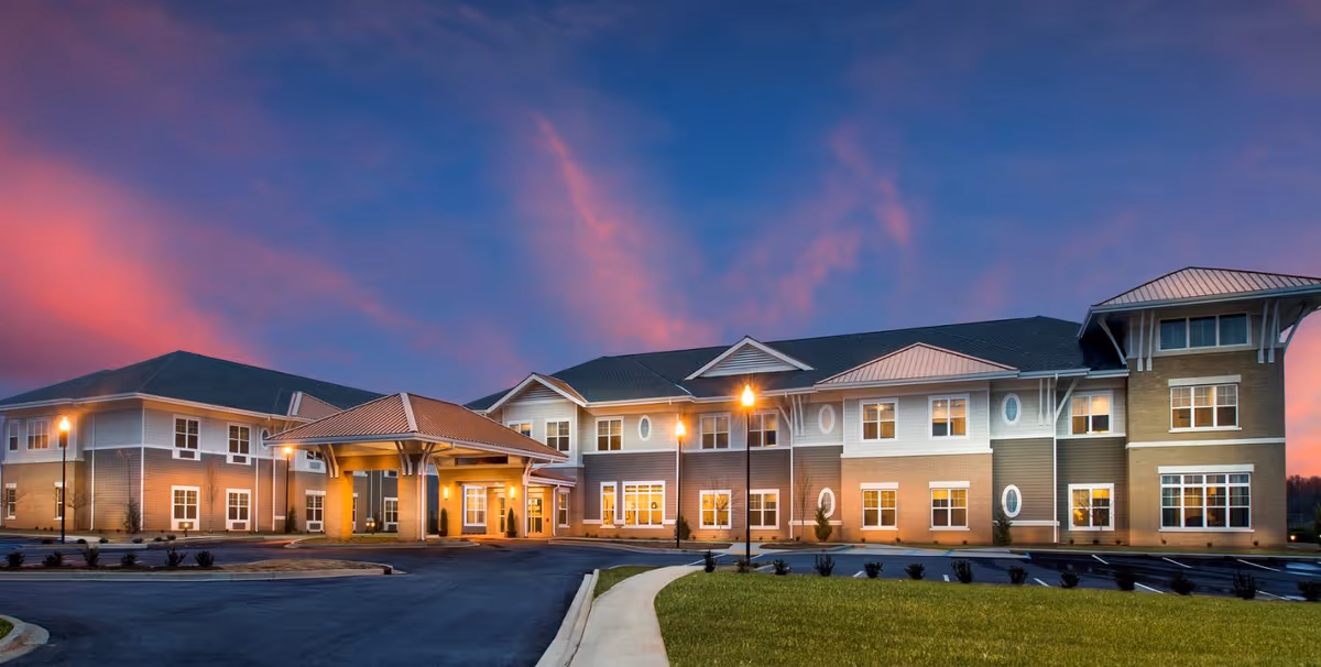 Front exterior view of a two-story senior living building with a lit covered entrance at dusk.