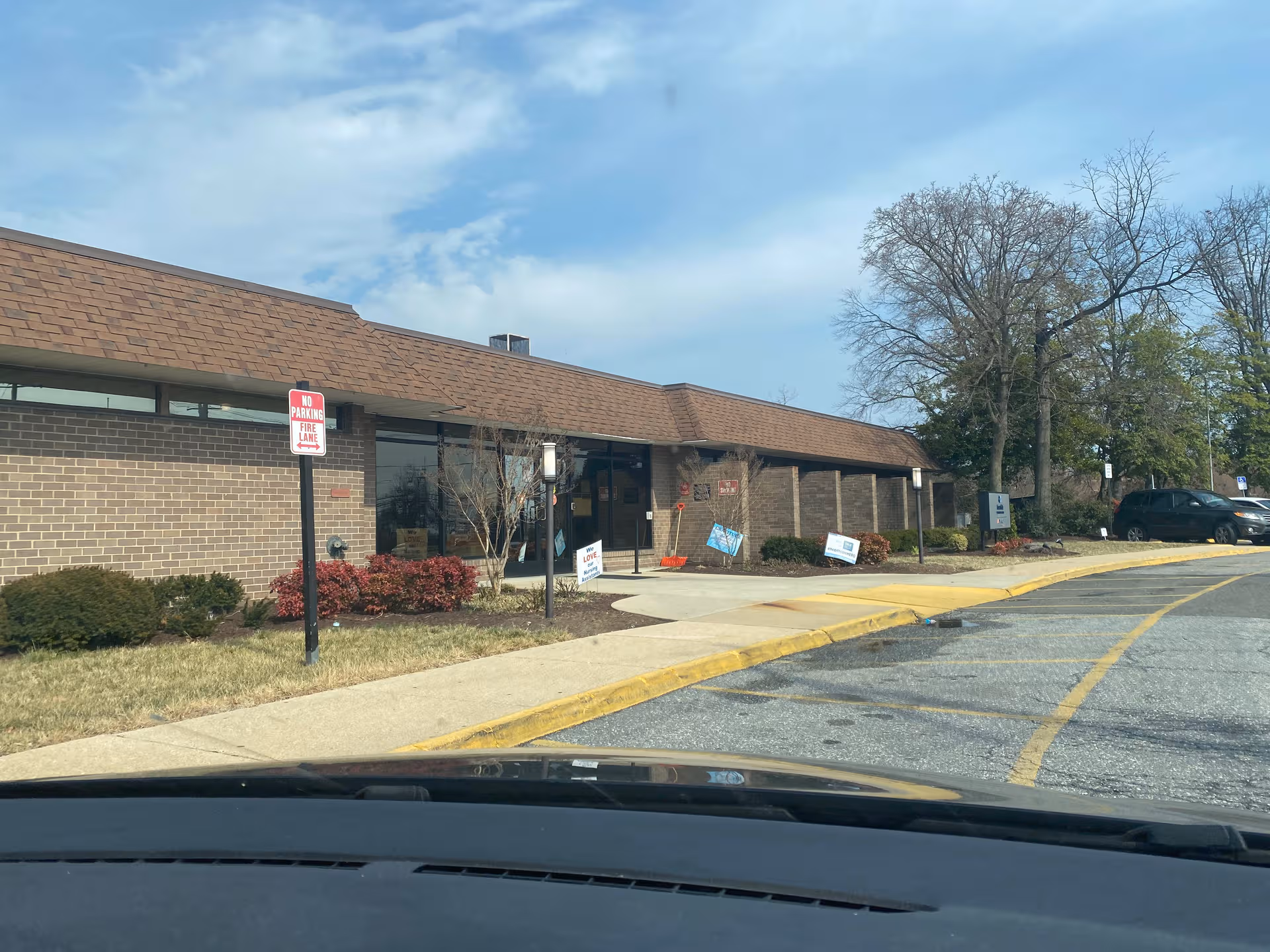 Single-story brick senior care facility exterior with parking and leafless trees.