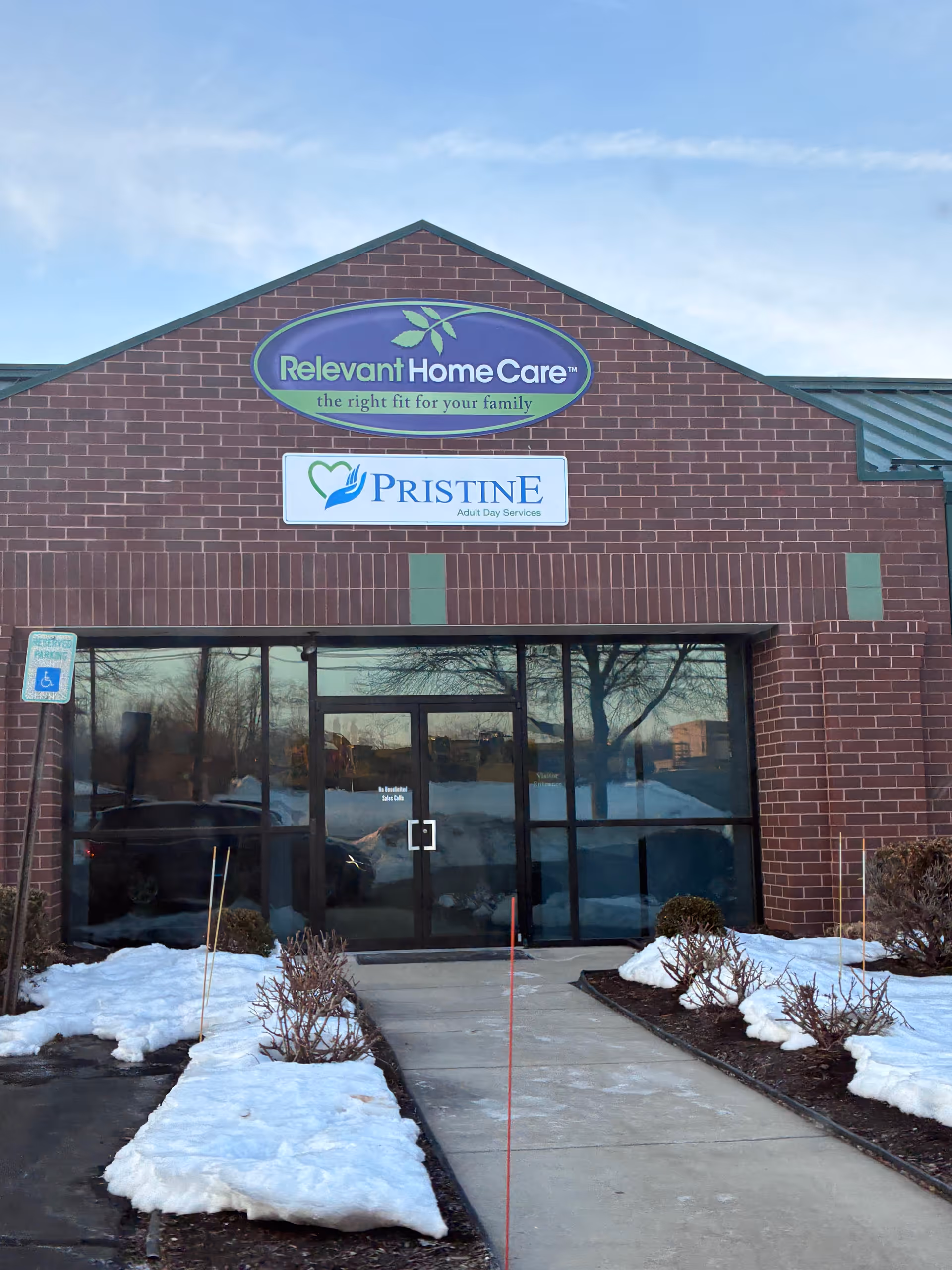 Brick facility entrance with Relevant Home Care and Pristine signs, snowy ground.