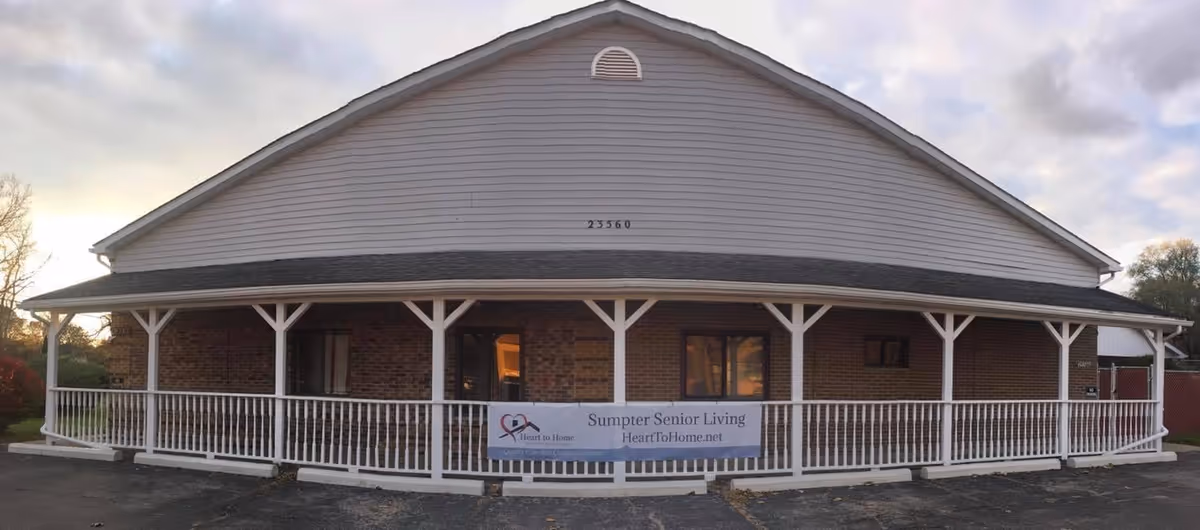 Front view of a single-story brick senior living building with a white wraparound porch.