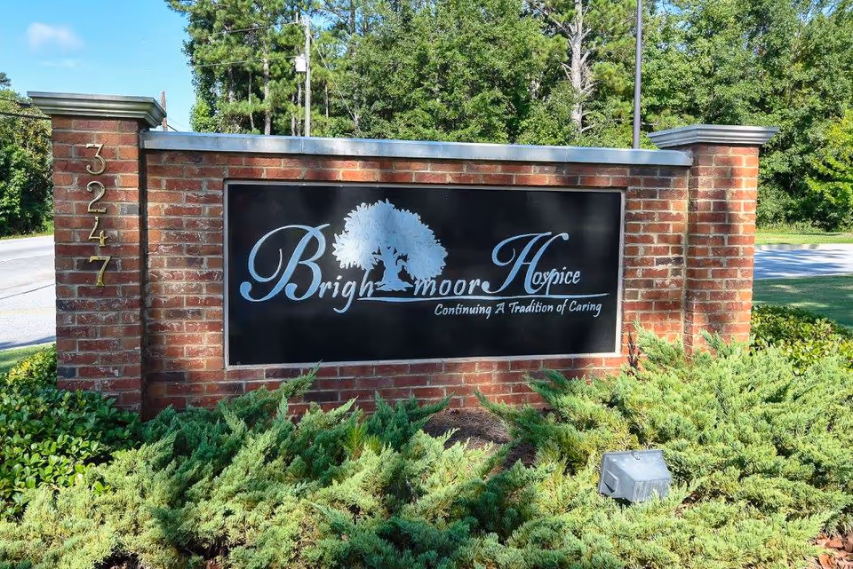 Brick entrance sign for Brightmoor Hospice with tree logo, framed by green shrubs.