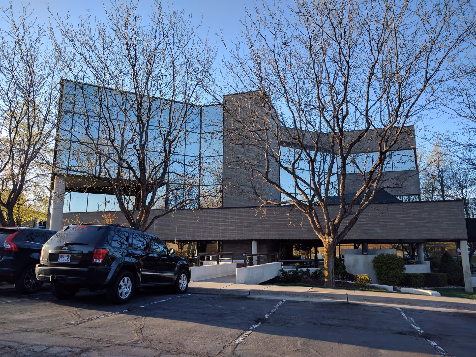 Modern glass-front senior care building with bare trees and parked cars.