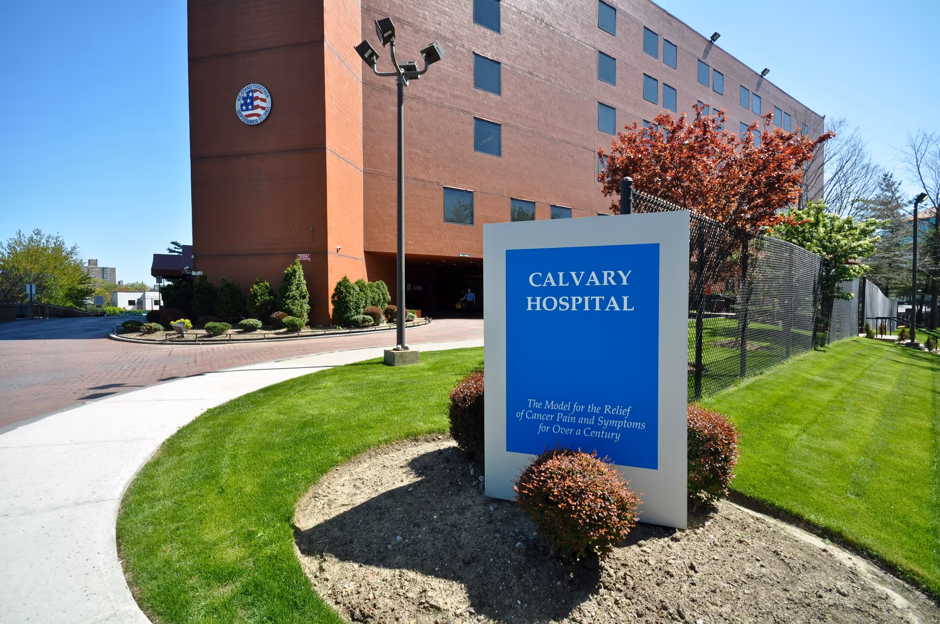 Red brick hospital building with a blue Calvary Hospital sign in a landscaped front yard.