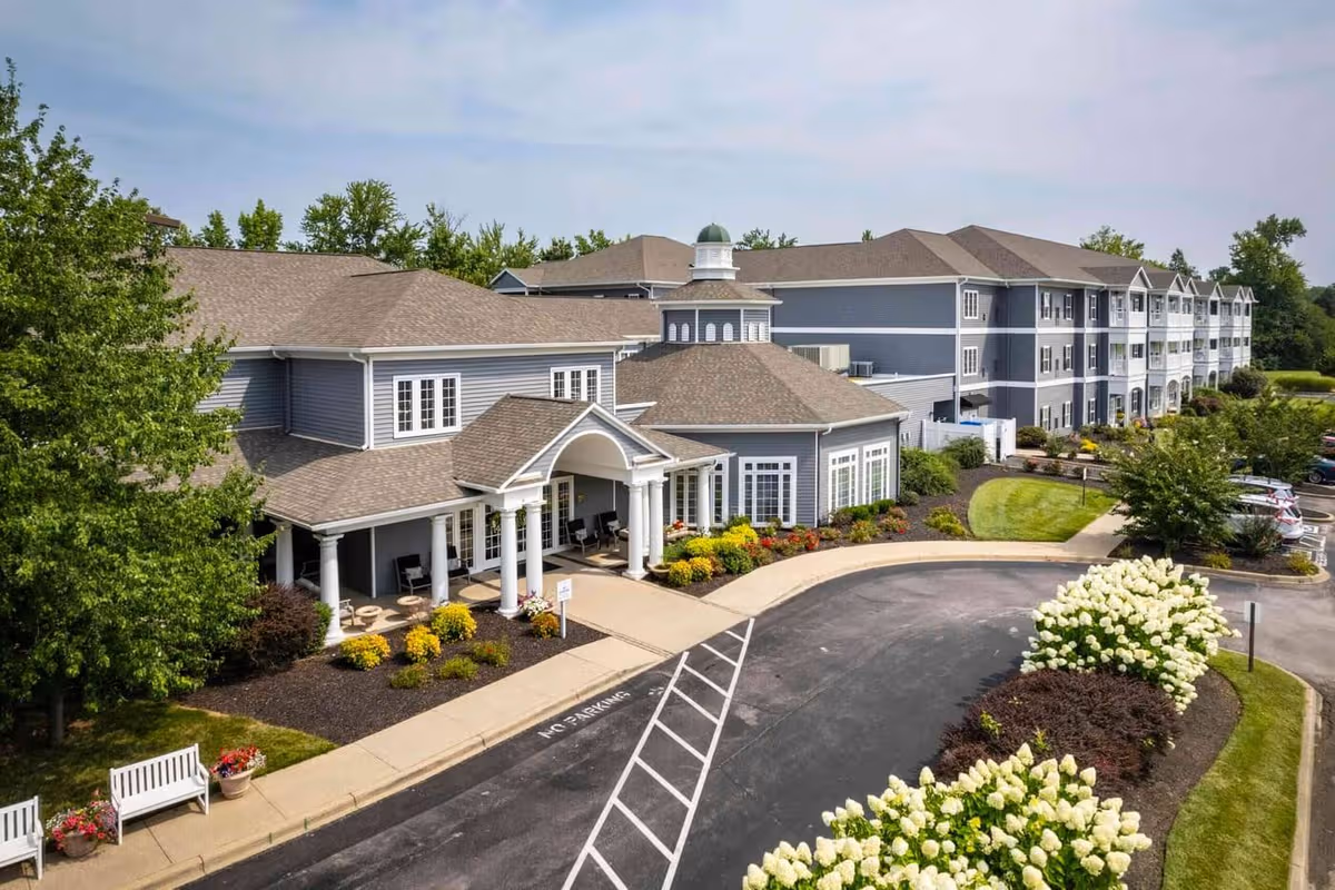 A large blue-gray senior living facility exterior with curved driveway and landscaped entrance.