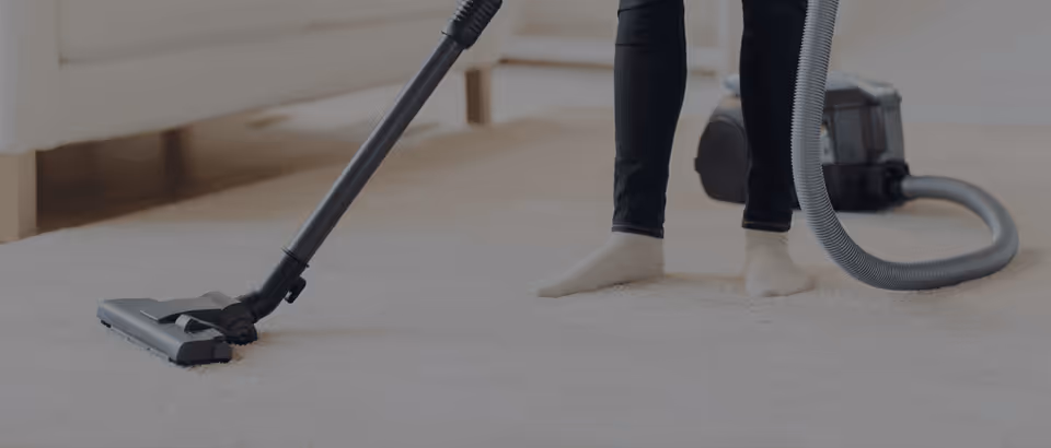 A person vacuuming a carpet in a living room at a senior care facility.