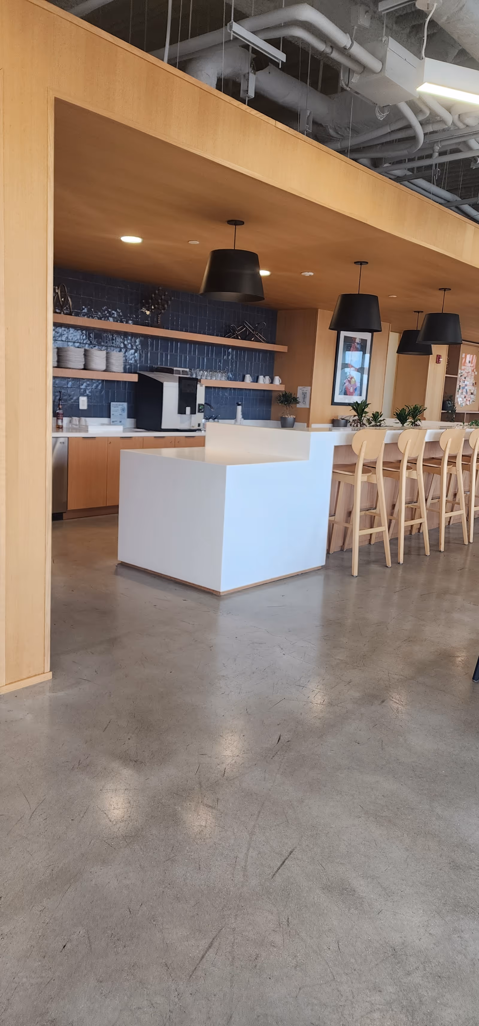 A modern cafe-style dining area with a white island, wooden stools, blue tiled backsplash, pendant lights.