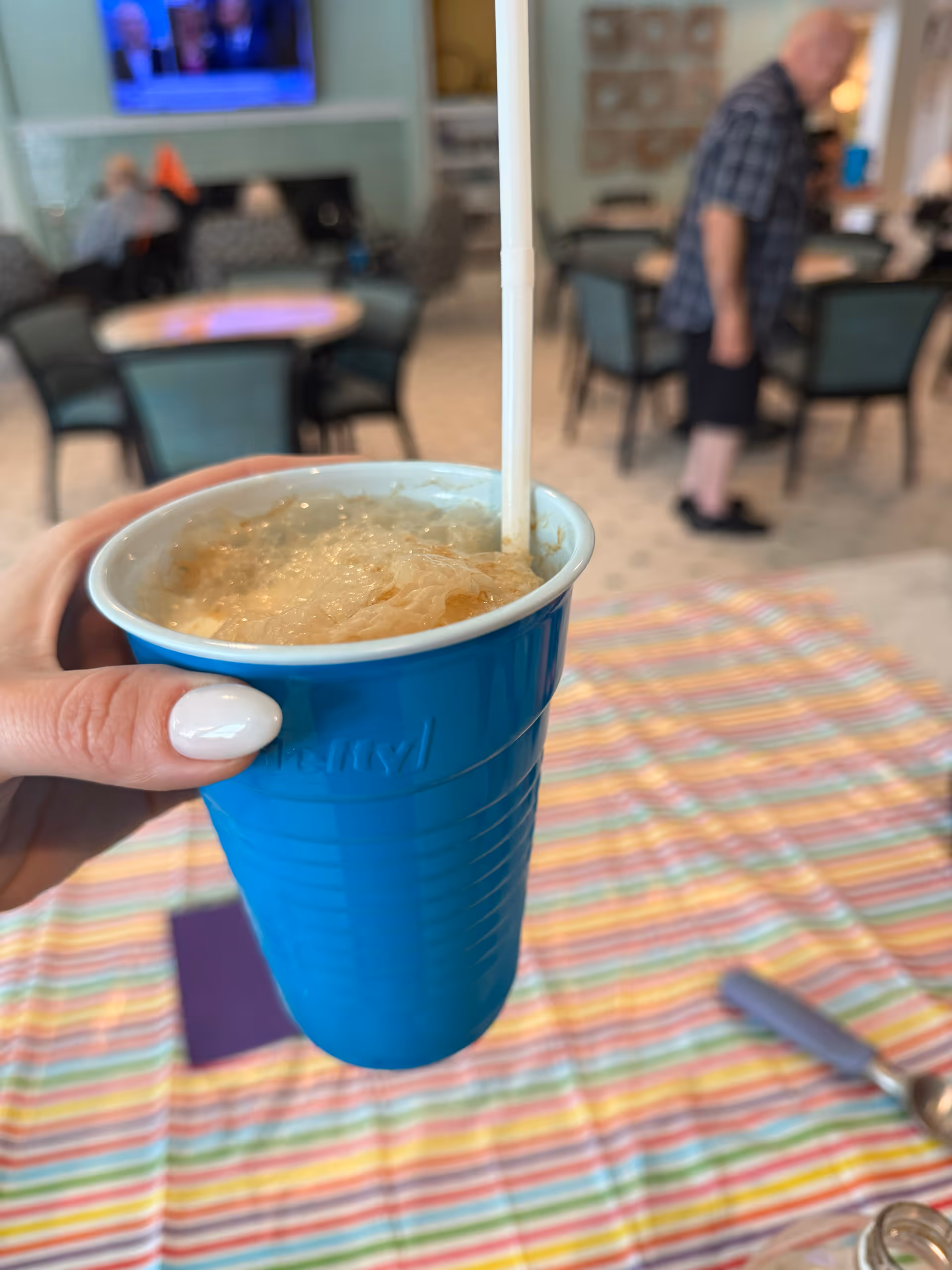 A hand holds a blue cup with ice in Concierge Care dining area.