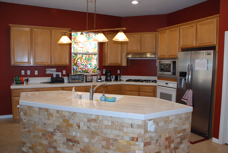 Spacious kitchen with an island, wood cabinets, red walls, and stainless appliances.