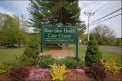 Exterior view of River Glen Health Care Center sign amid landscaped shrubs and trees.