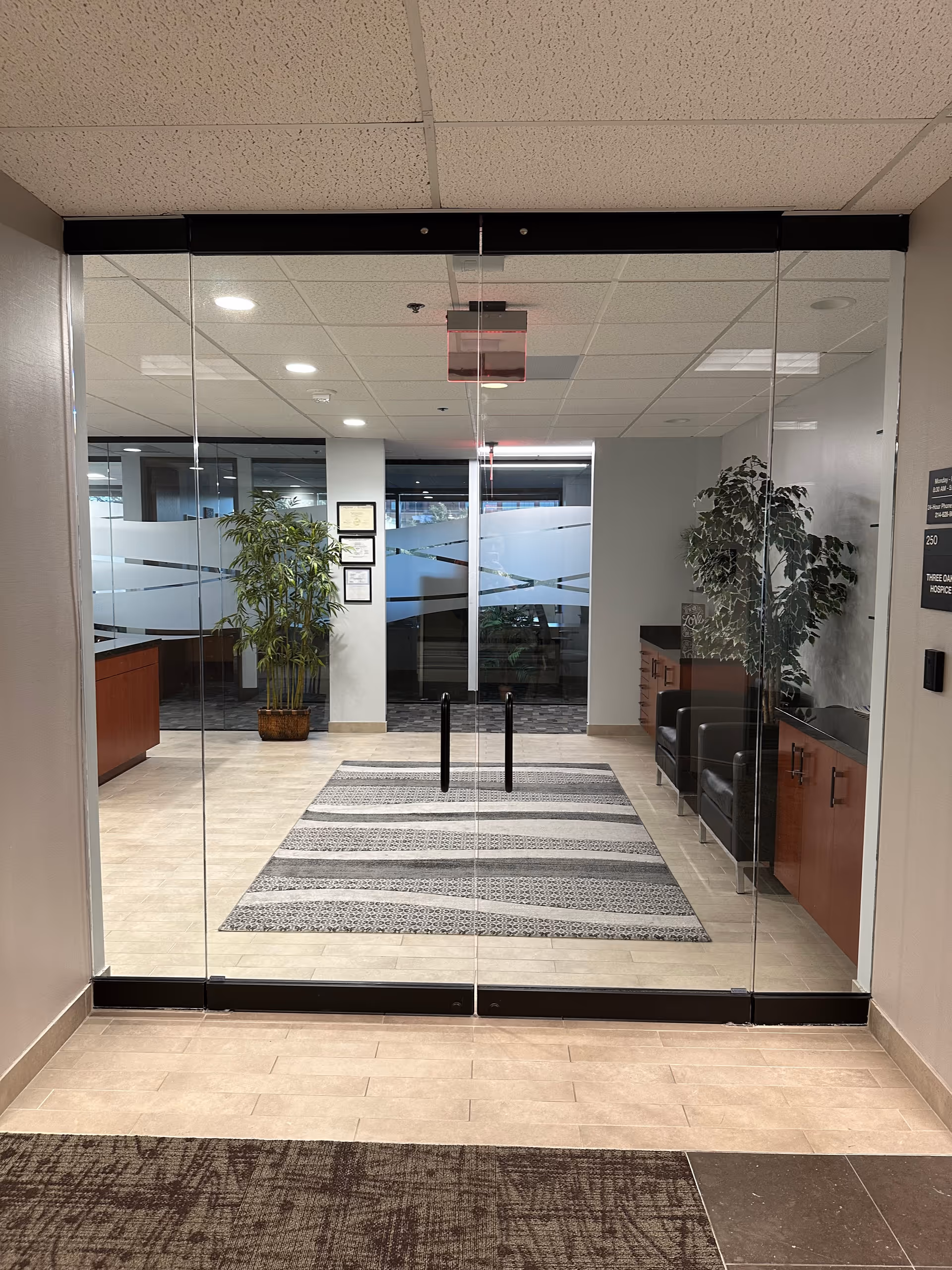 Glass doors reveal a bright lobby with seating, plants, and a striped rug.