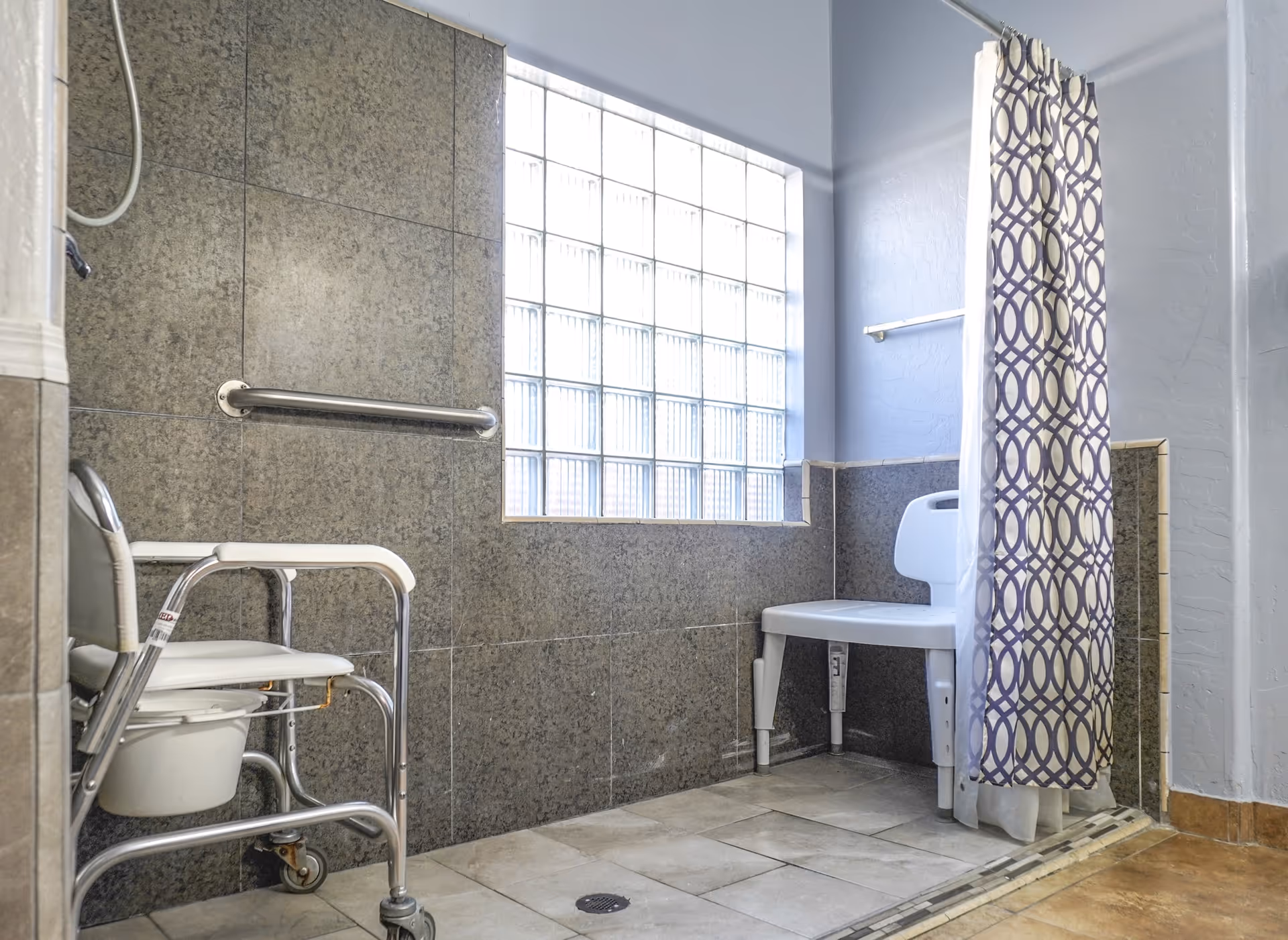 Accessible senior bathroom with a shower bench, walker, and patterned curtain.