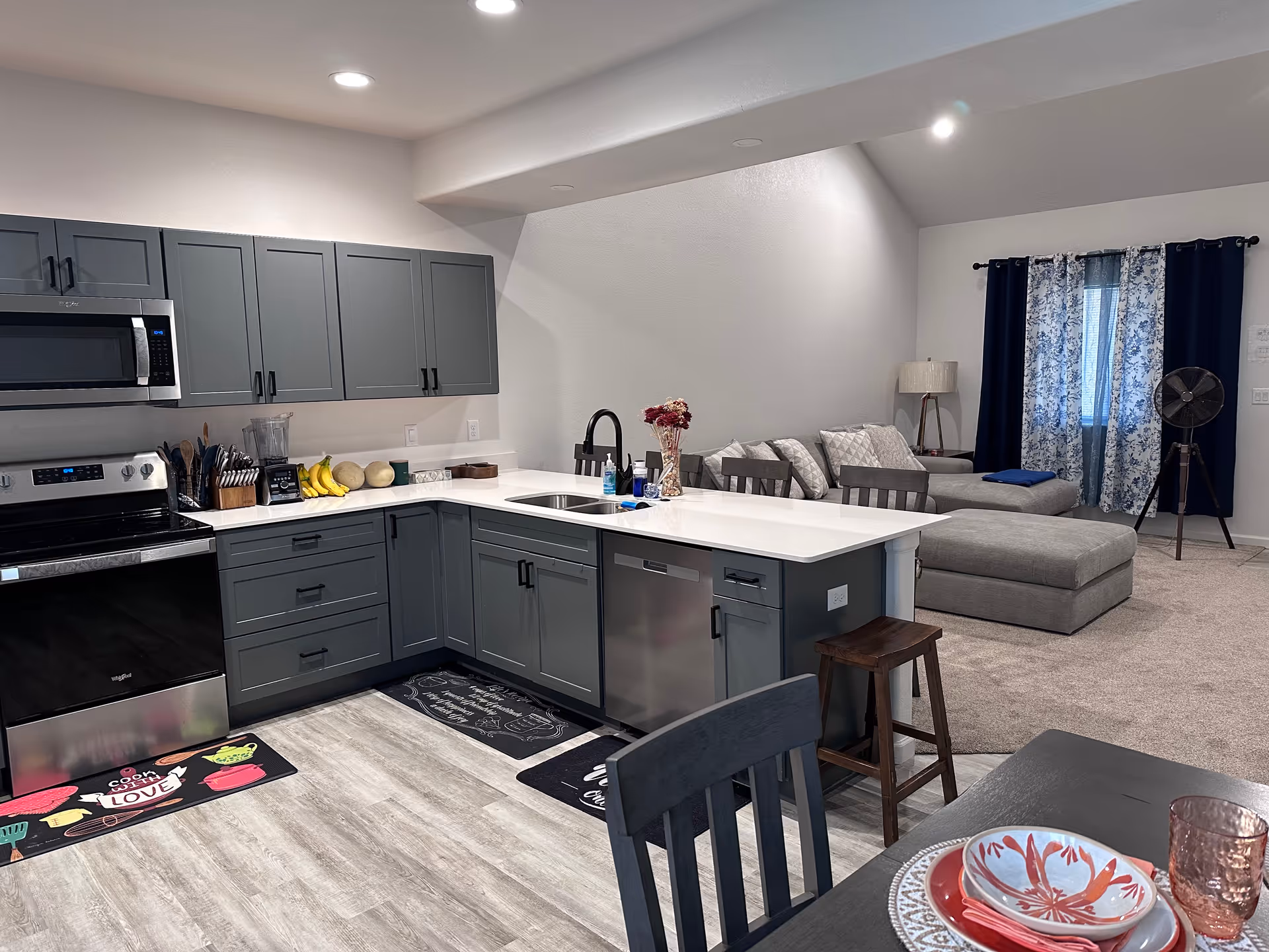 Open-plan kitchen and living area in a senior living facility with gray cabinets and sofa.