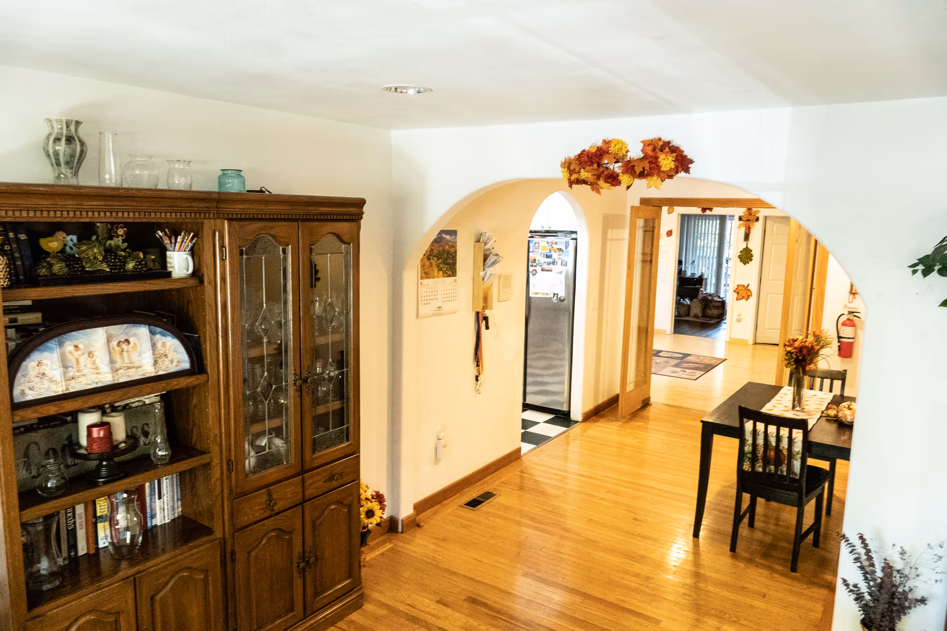 Wood-floored dining area with an arched doorway, wooden cabinet, and a flowered table.