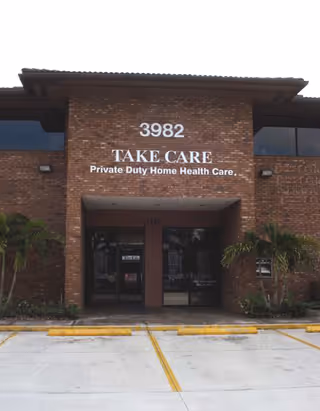 Brick building with Take Care sign and entrance doors, driveway in the foreground.