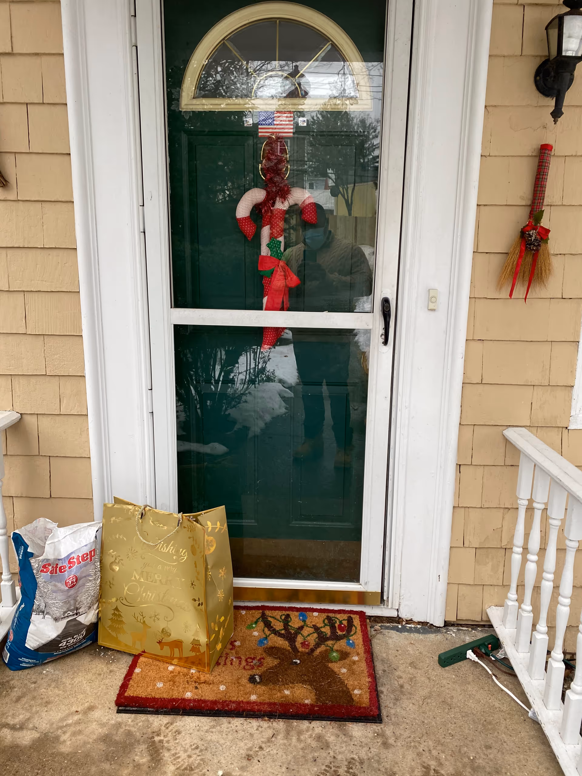 Front door entrance with holiday wreath, bags on a festive doormat, beige siding.