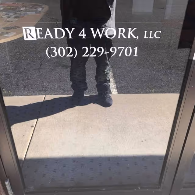 Reflection of a person standing outside a glass door with Ready 4 Work sign.