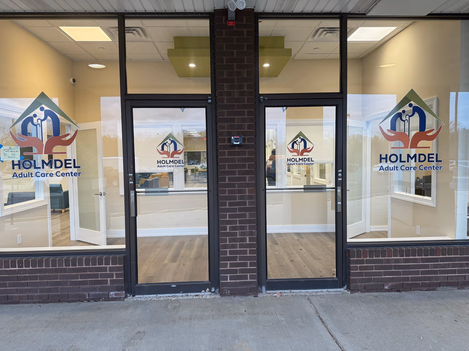 Glass storefront of Holmdel Adult Care Center with logos and double doors.