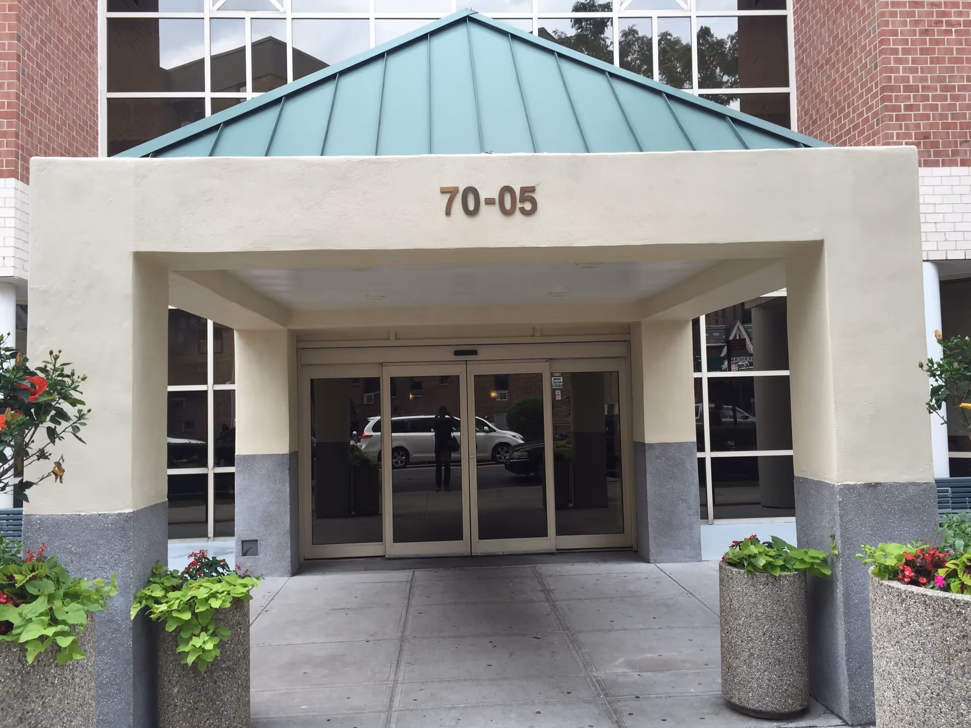 Entrance to a senior living facility with glass doors, a canopy, and planters.