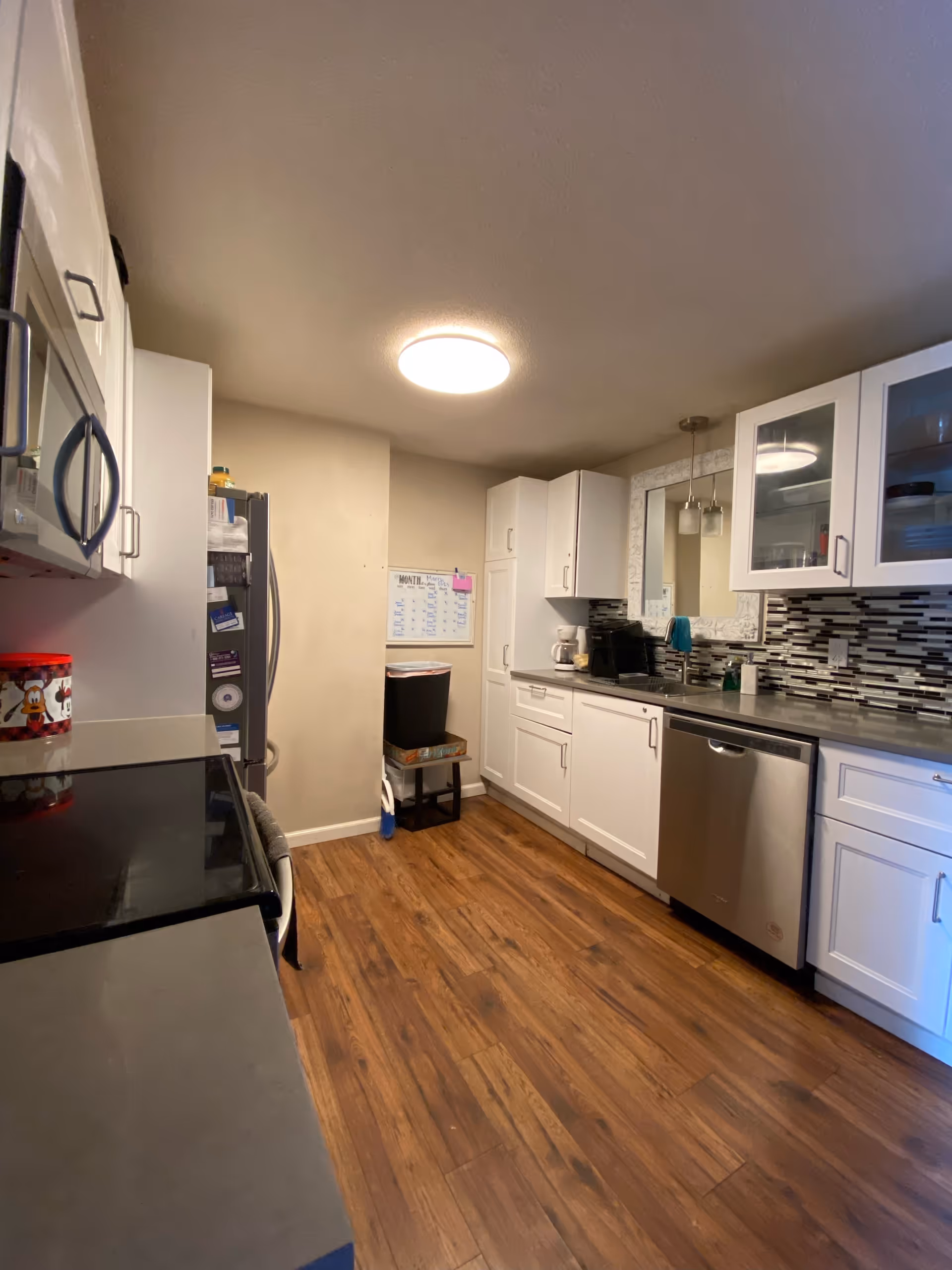 Bright white kitchen with stainless appliances, tile backsplash, and wooden flooring.