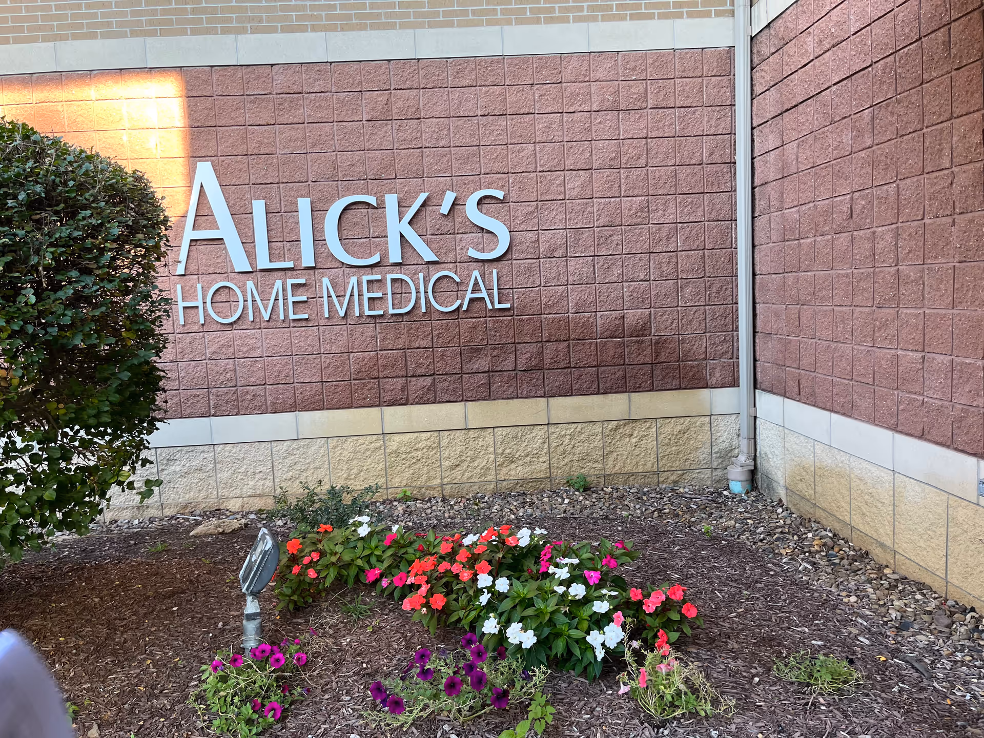 Exterior view of Alick's Home Medical building with a landscaped flower bed.