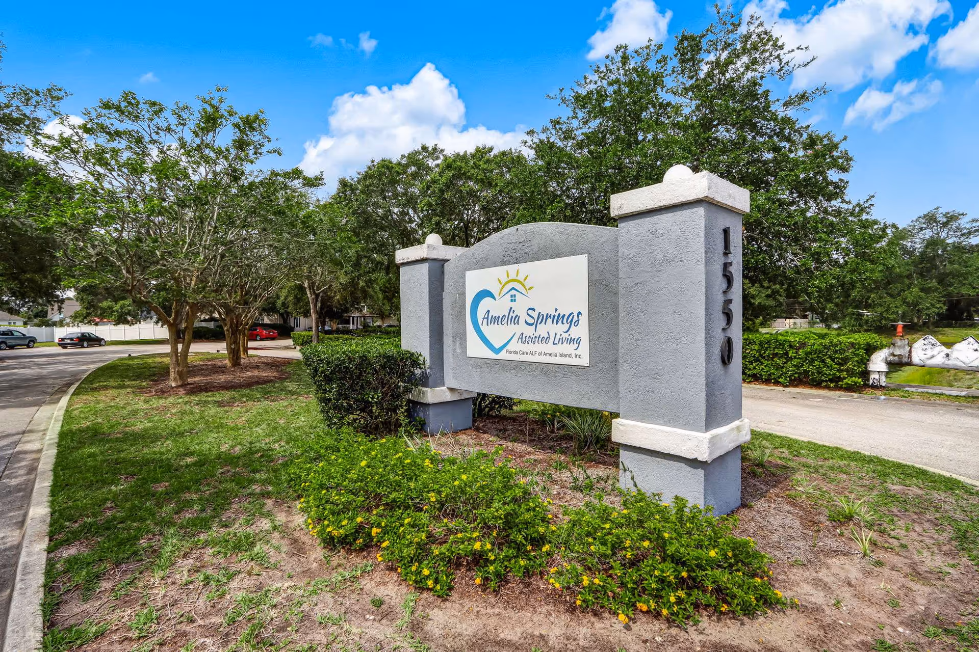 Exterior view of Amelia Springs Assisted Living sign with trees and landscaping at entrance.