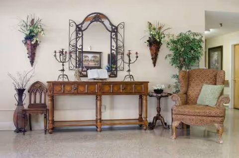Elegant console table with mirror, plants, and a cushioned chair in a waiting area.