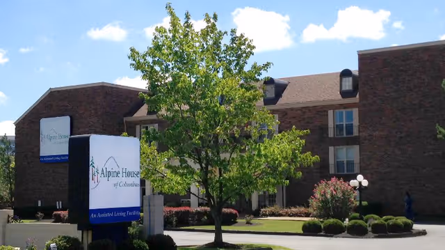 Exterior view of Alpine House of Columbus with a sign, tree, and brick building facade.