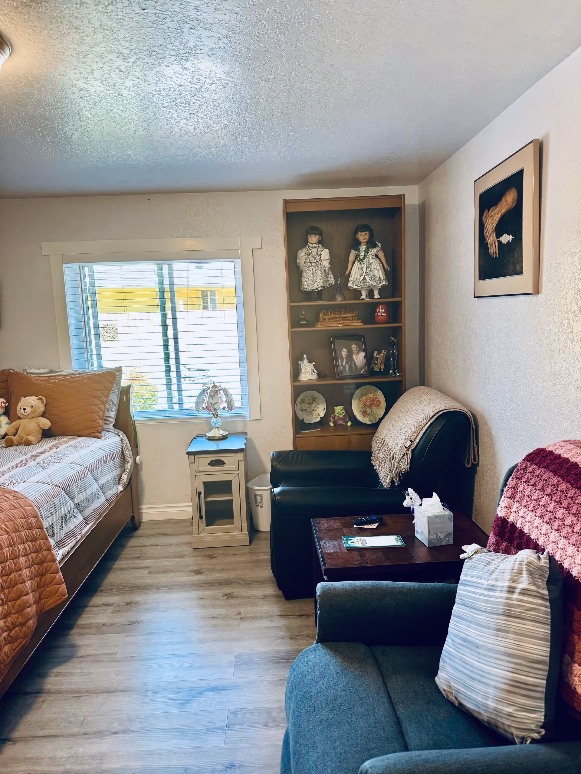 Cozy bedroom featuring a bed, leather chair, display cabinet, window, and teddy bear.
