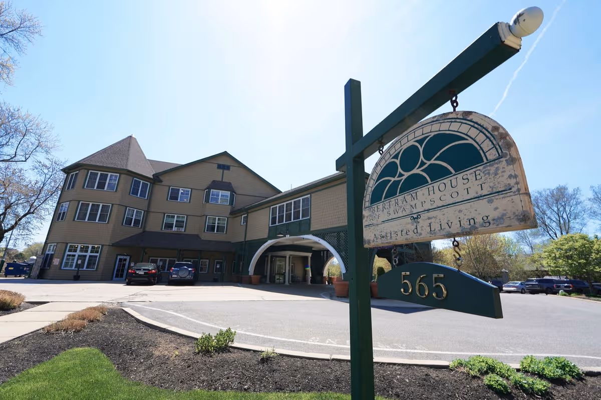 Exterior view of Bertram House of Swampscott assisted living facility with sign and parking lot.