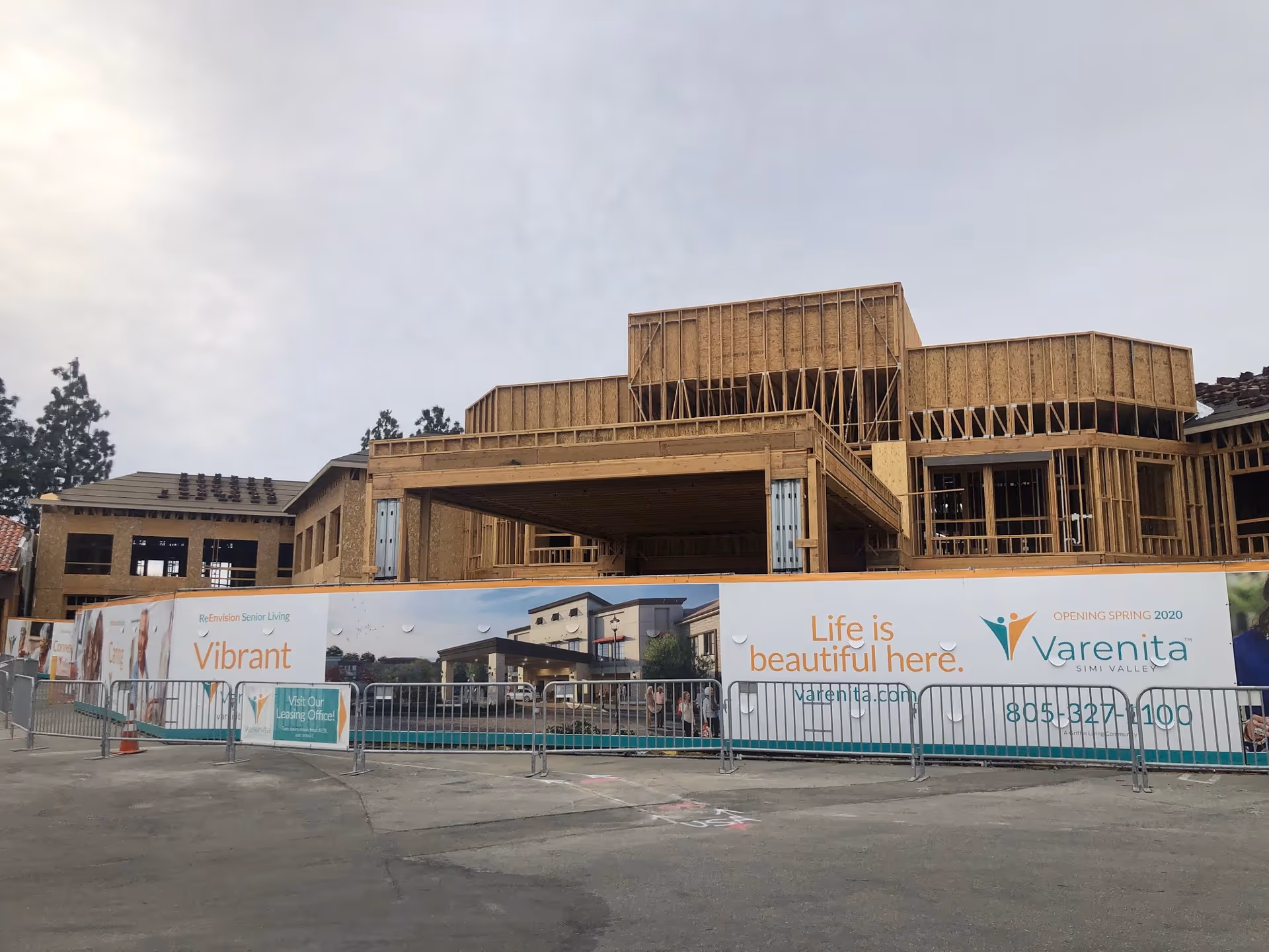 Under-construction senior living building with exposed wood framing and banners along a metal fence.