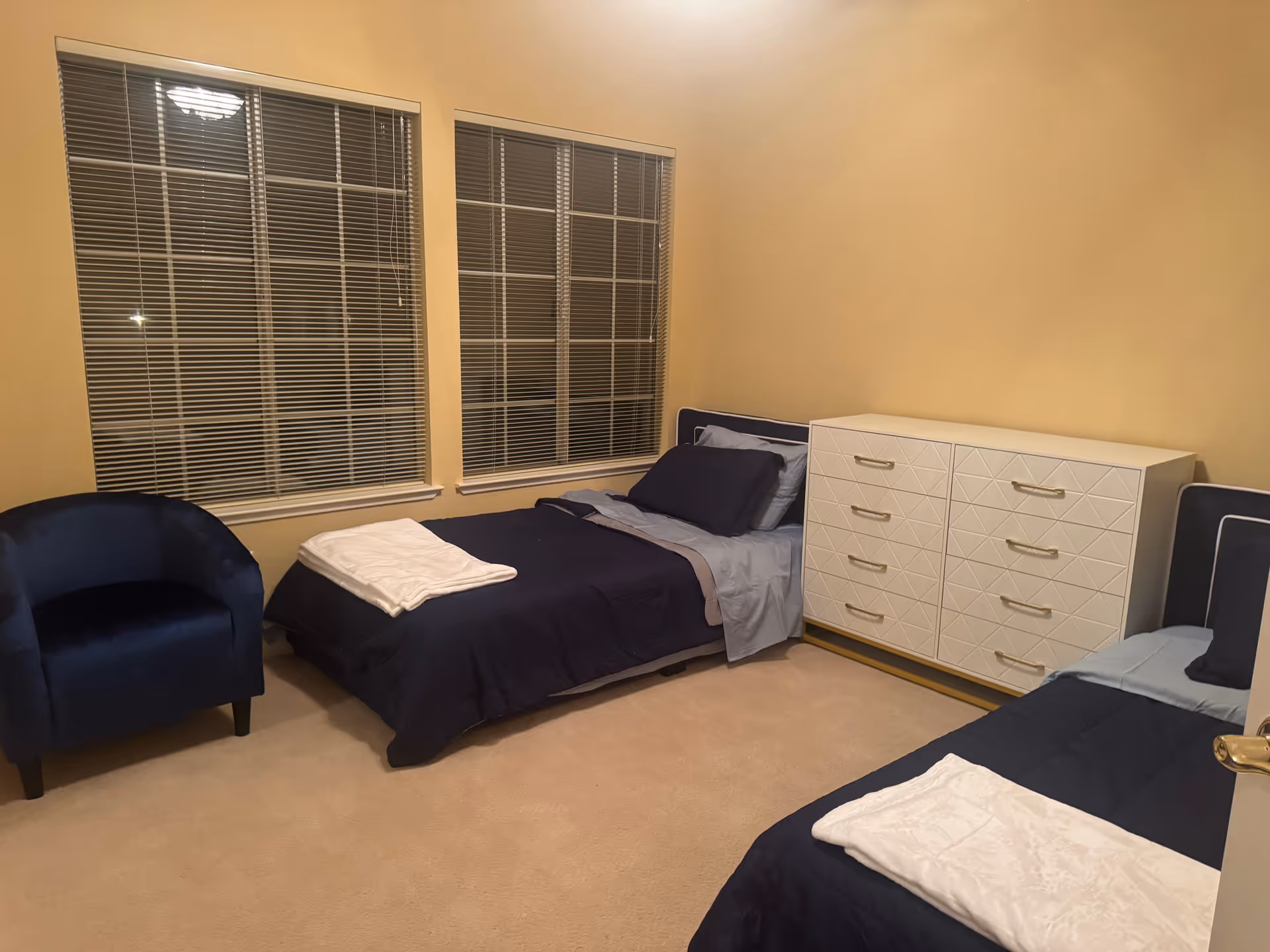 Two twin beds with navy bedding and a white dresser in a beige bedroom.