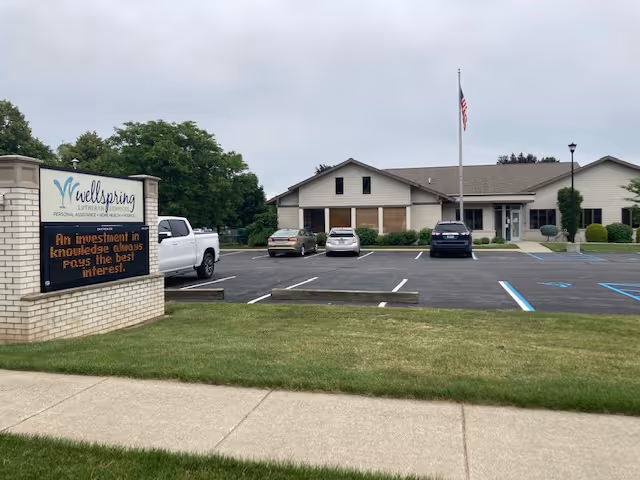 Exterior view of Wellspring Frankenmuth Hospice building with parking lot and sign.