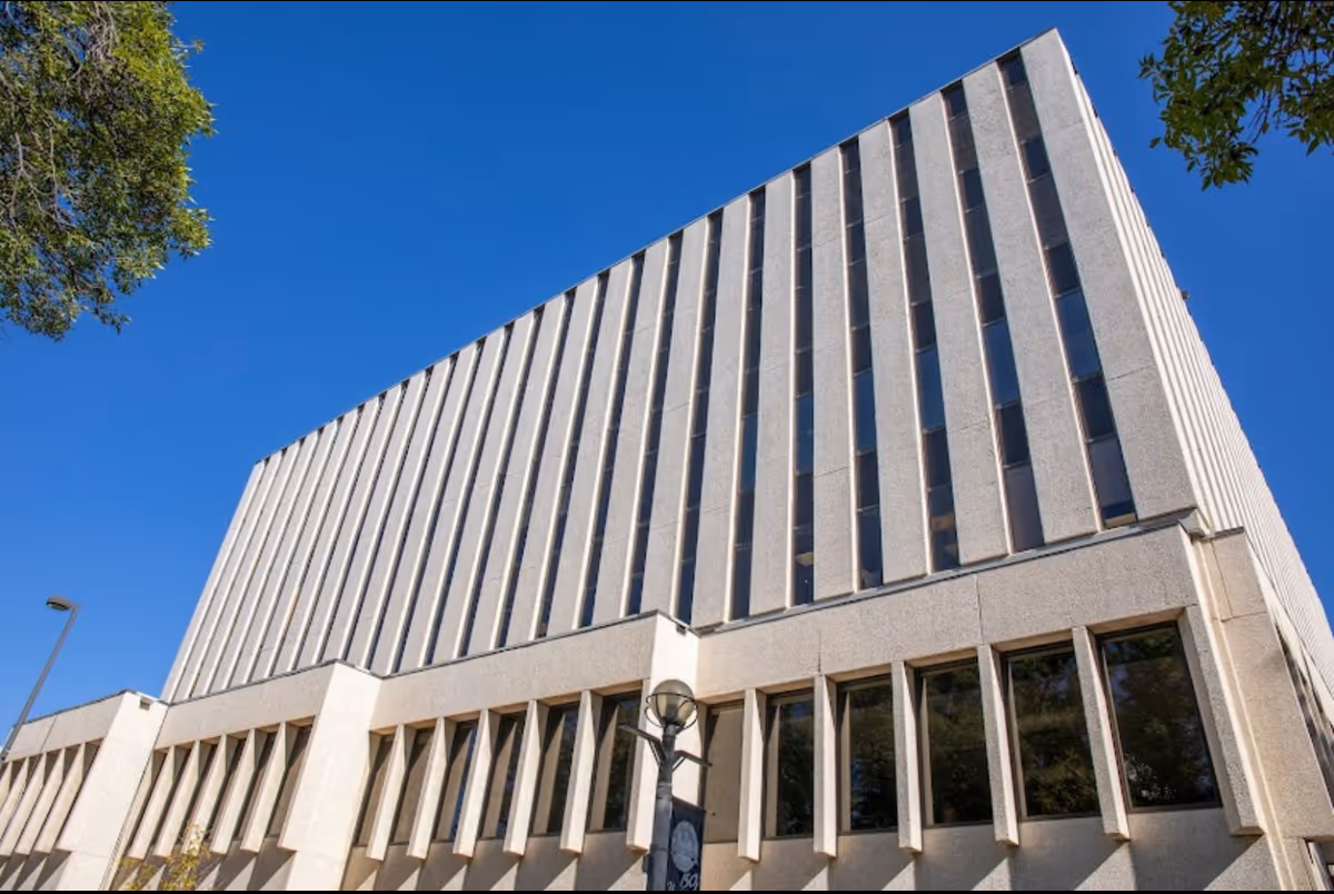 Modern multi-story building exterior with vertical concrete fins and large window panels.