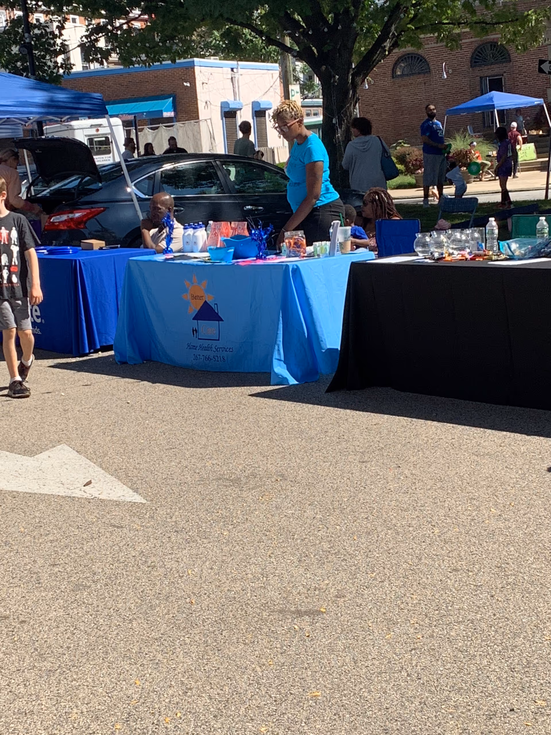 Outdoor street fair with blue tablecloths and people gathered around Better Care Home Health Services booth.