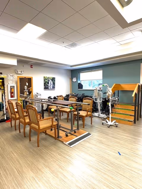 Therapy gym with parallel bars, exercise machines, and wooden chairs inside Senior TLC.