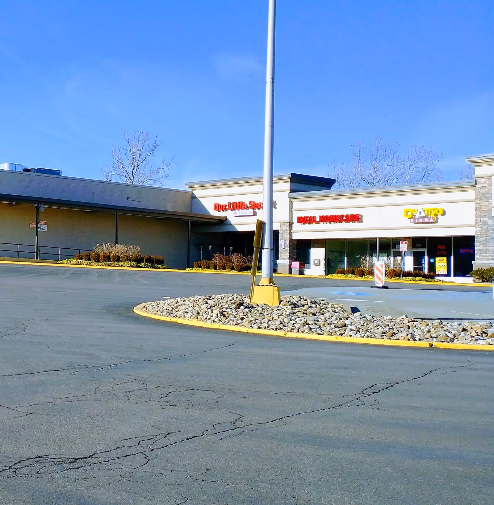Exterior view of a strip mall with a circular rock median and parking lot.