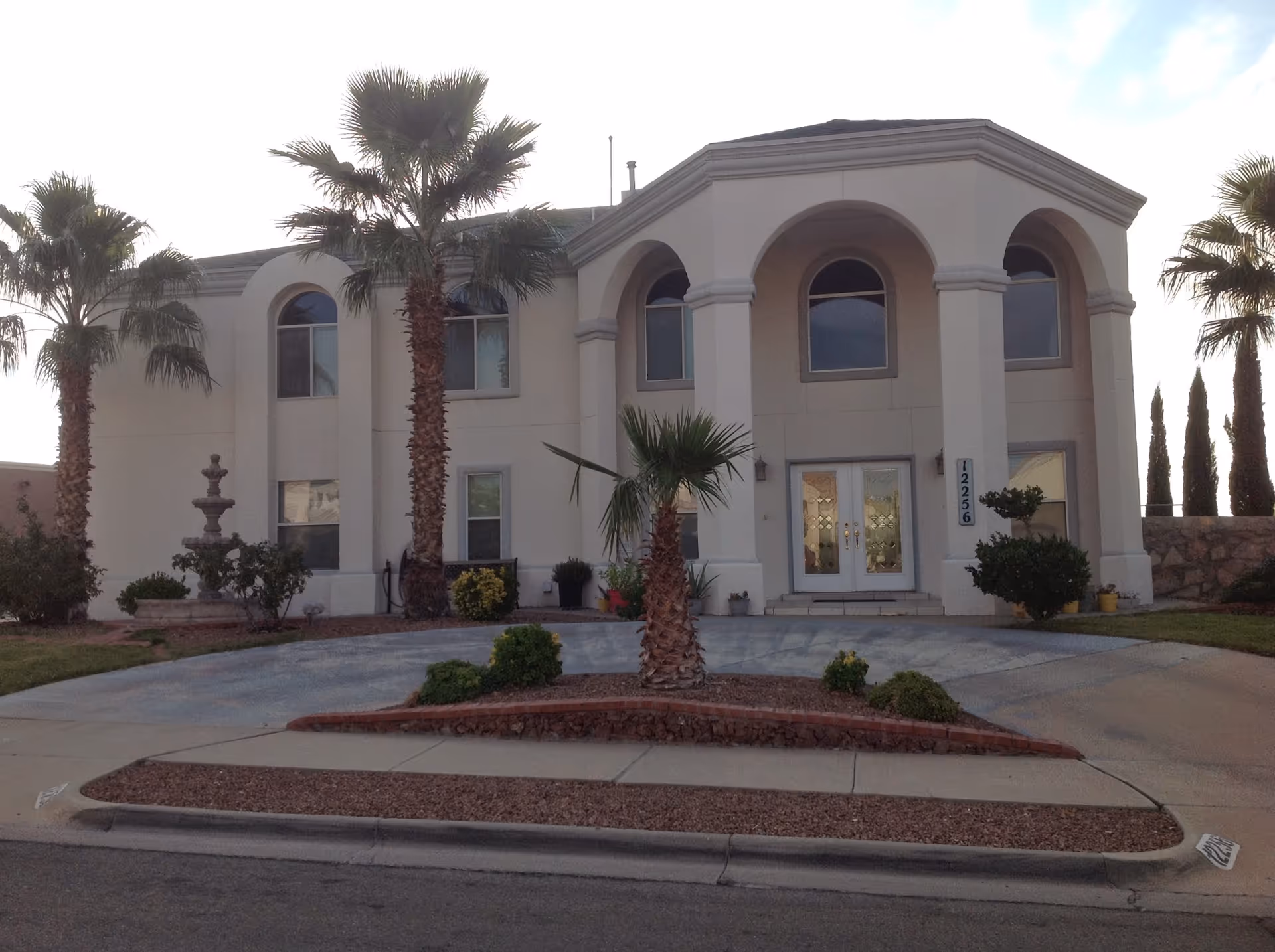 Front view of Angel's Heaven Adult Foster Home, a beige building with palm trees and entryways.