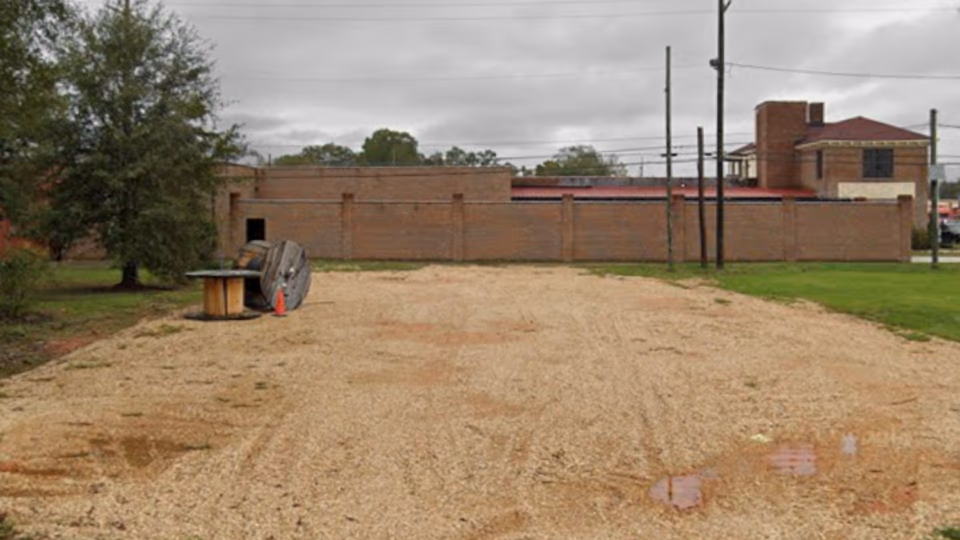 Gravel lot outside a brick facility with a long wall and utility poles.