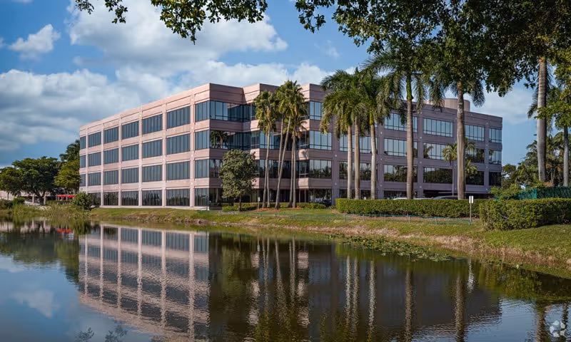 Exterior view of a pink multi-story building with palm trees reflected in a water canal.
