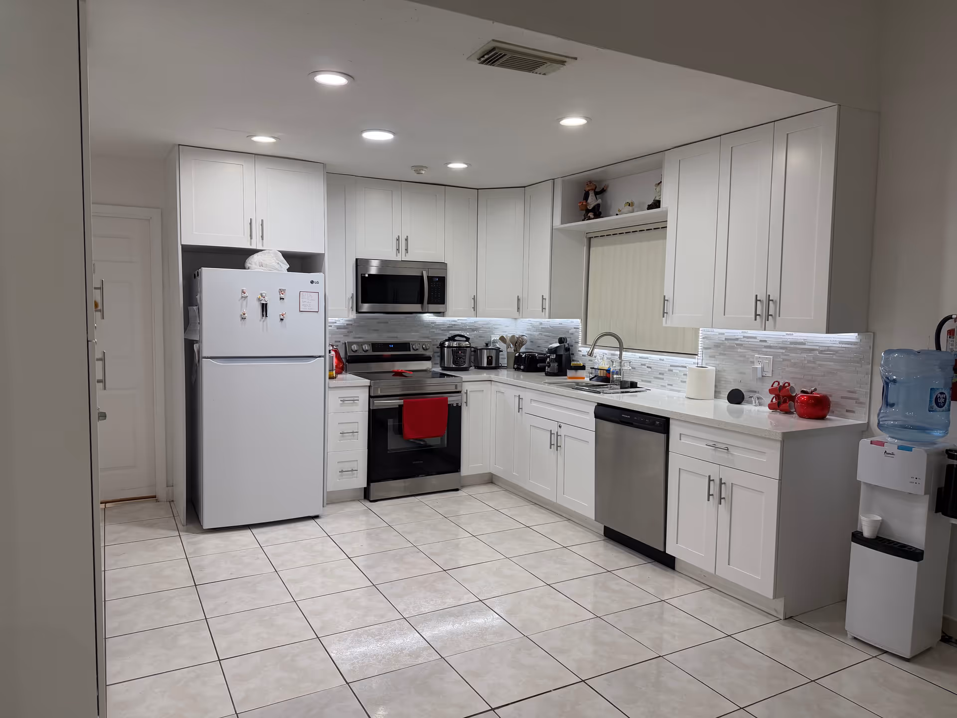 Bright white kitchen with appliances, cabinets, a sink, and a tiled floor.