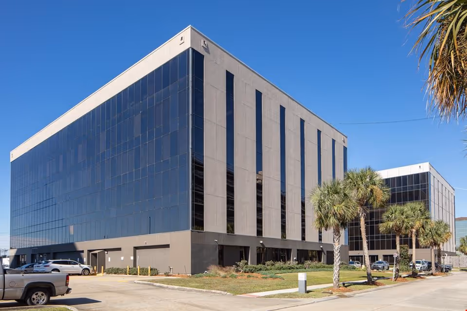 Notre Dame Hospice building with a glass facade and palm trees along the parking area.