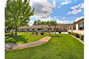Exterior courtyard of Skyline Transitional Care Center, with green lawn, trees, and curved brick pathway.
