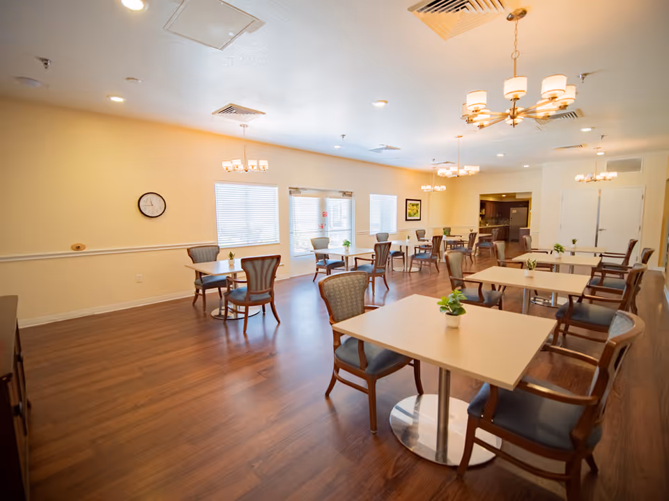 Bright dining room in a senior facility with multiple tables, chairs, and plants.