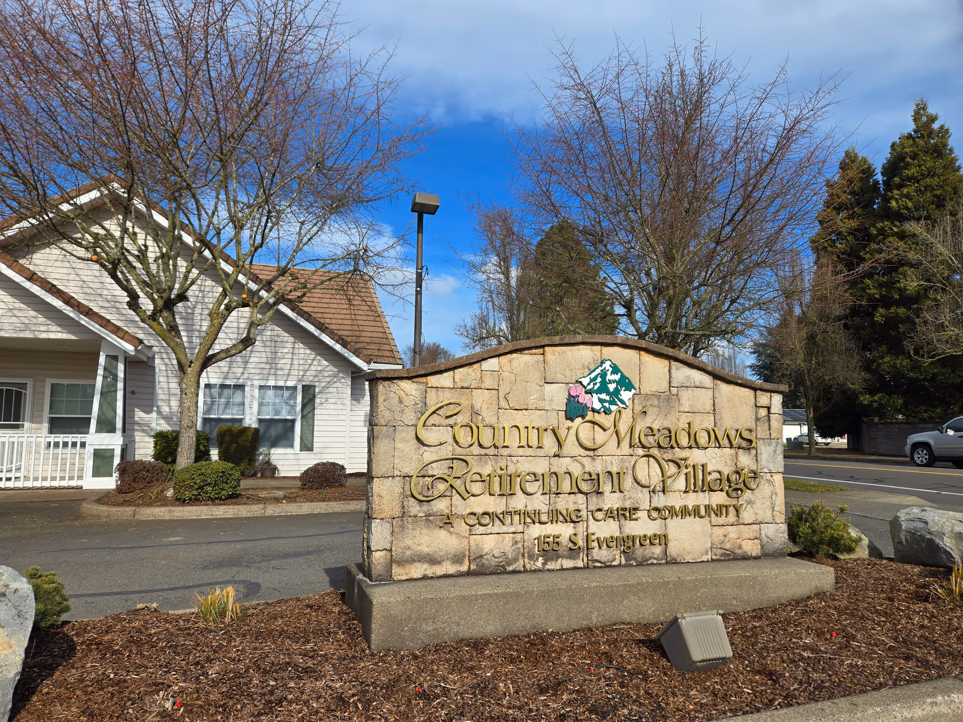 Stone sign reads Country Meadows Retirement Village with a building and trees in front