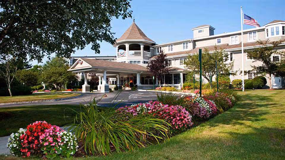 Exterior view of Heritage at Falmouth showing entrance, flag, and colorful flower beds.