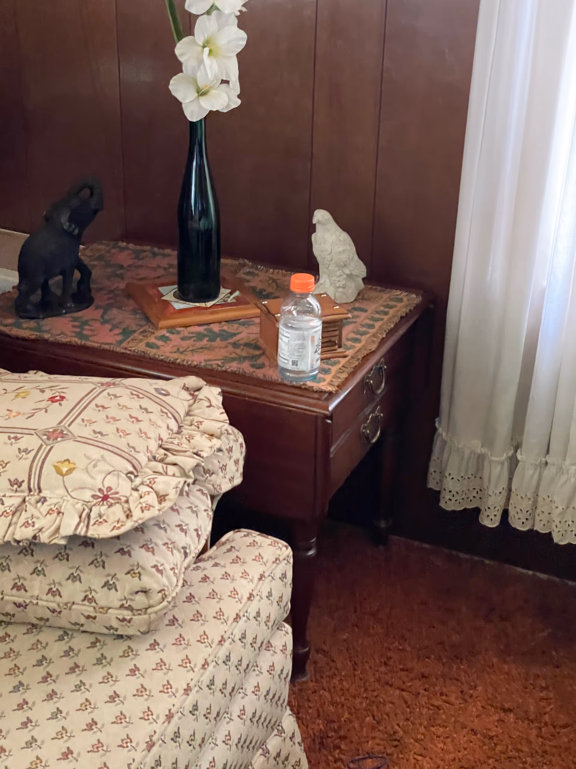 Wooden nightstand with decorative items beside a floral bed in a bedroom.