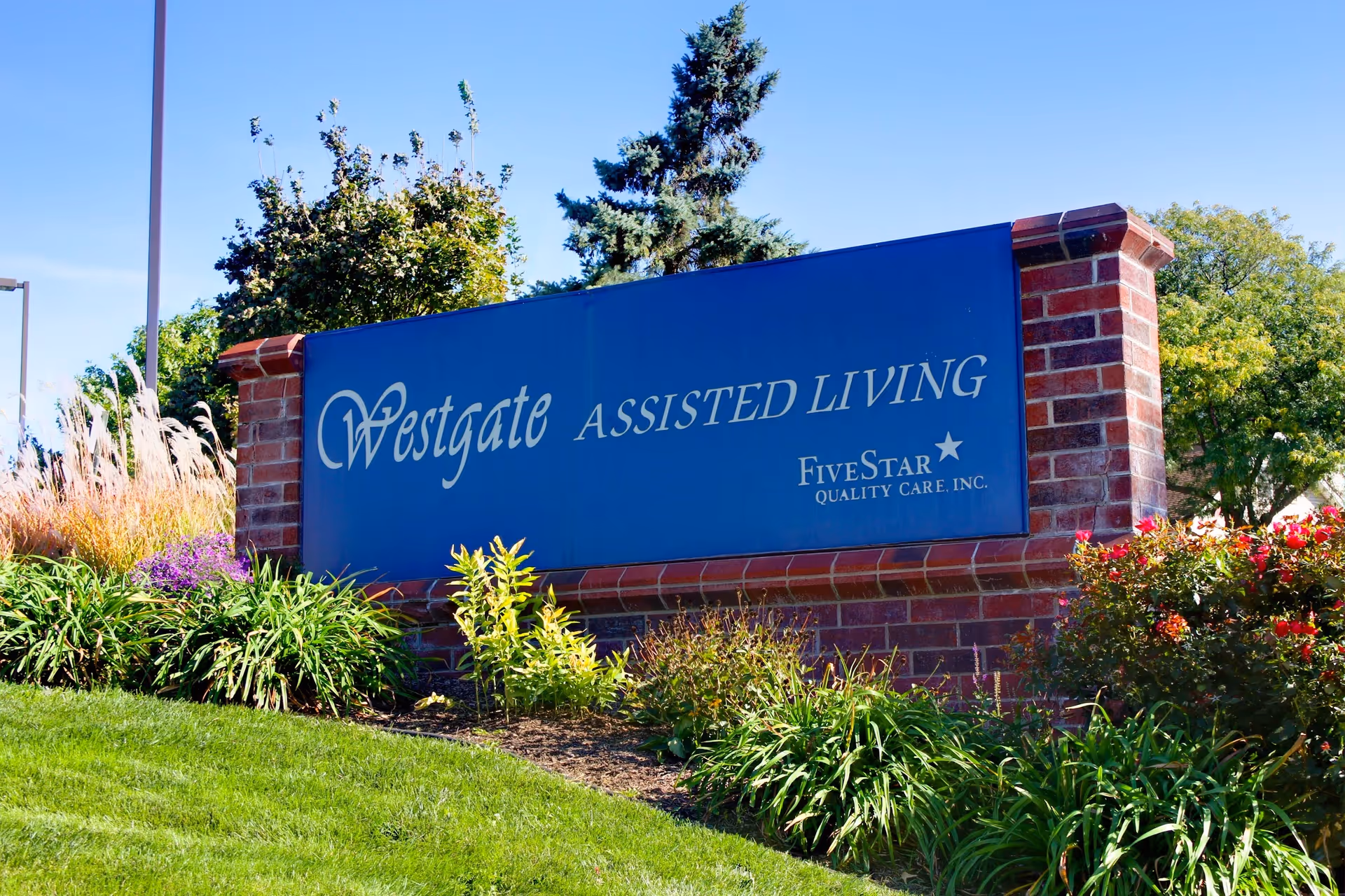 Blue Westgate Assisted Living sign on brick wall with surrounding landscaping