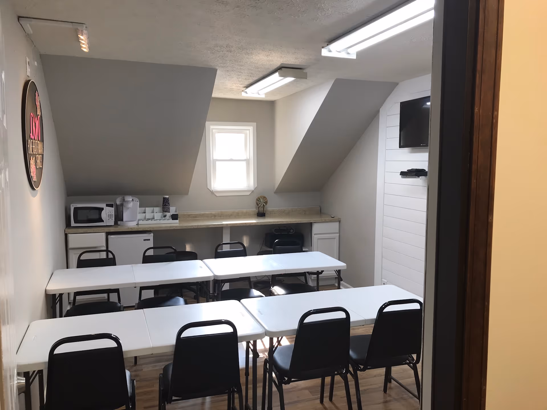Small dining area with white tables, black chairs, and kitchenette appliances along the back wall.