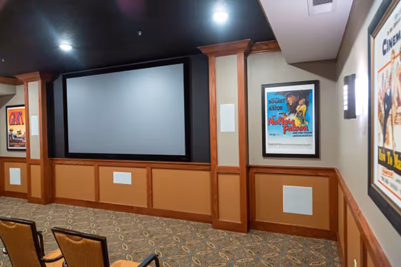 Senior living facility theater room with large screen, wood paneling, posters, and seating.