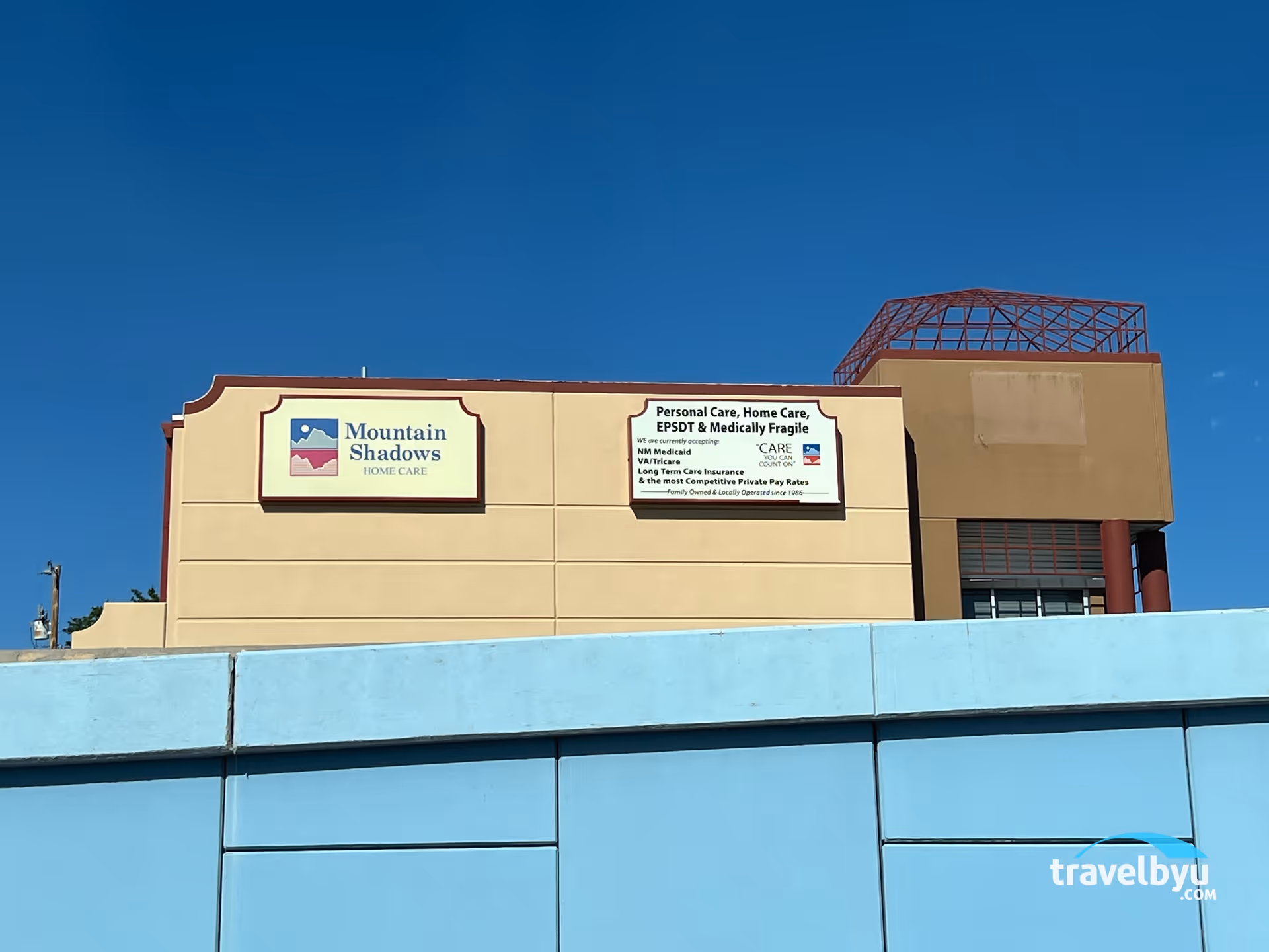 Exterior view of Mountain Shadows Home Care building with signs on beige wall and blue facade.